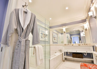 A resort room bathroom with glass shower stall, deep soaking tub, double vanity and cozy robe.